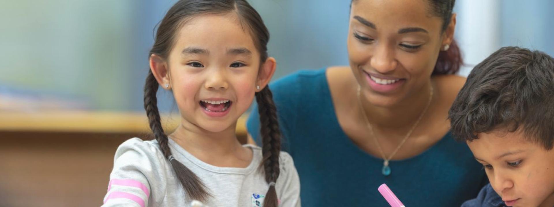 Girl smiling while another child works next to her