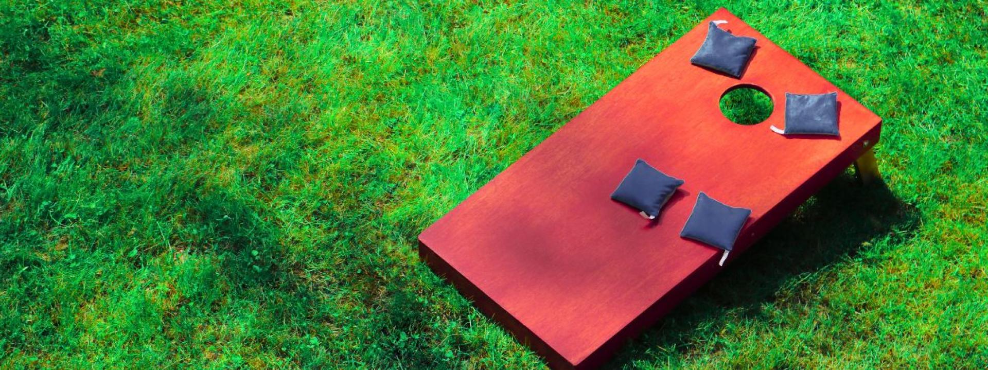 A cornhole board with bean bags on top of it sitting in grass