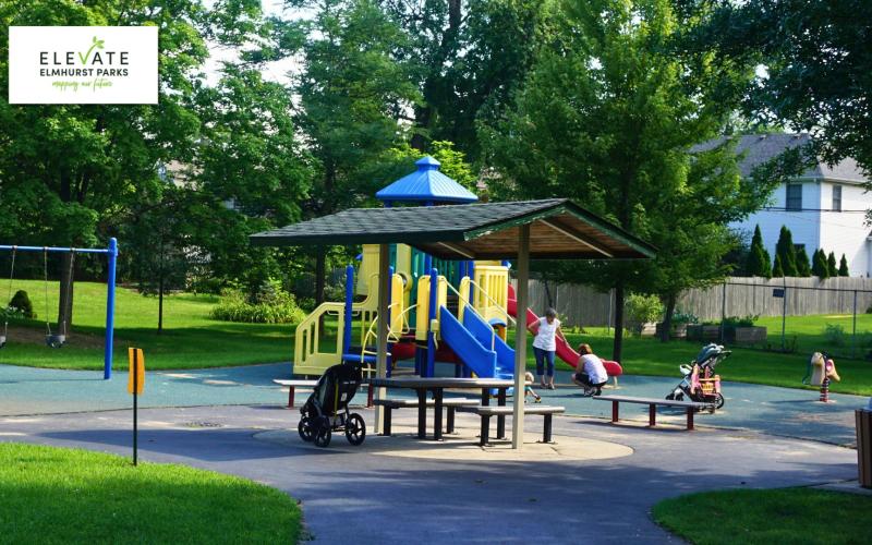 A playground with a colorful climbing structure, slides, swings, and picnic tables surrounded by green trees and grass.