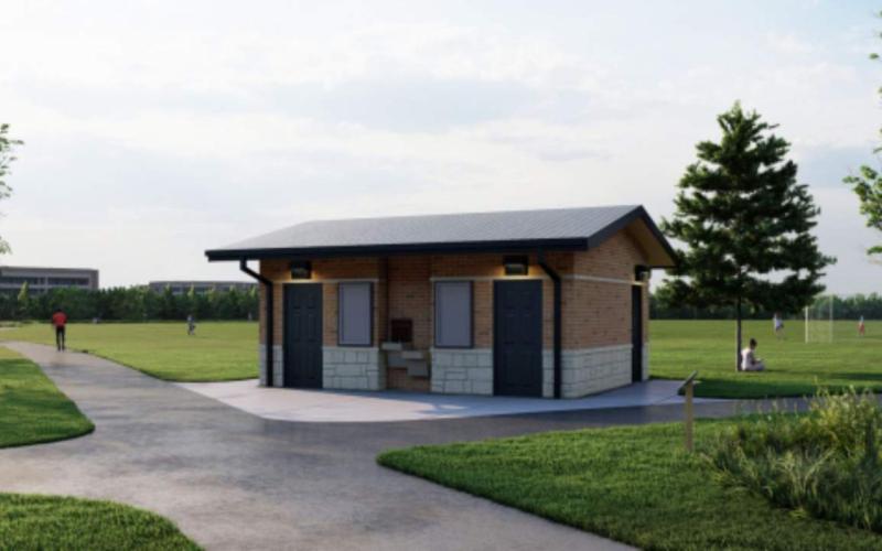 A brick restroom building with two dark doors, a water fountain and billboards