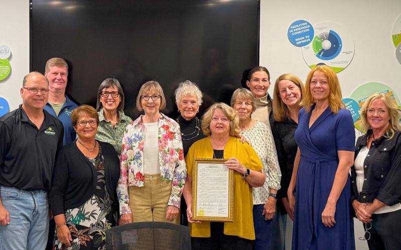 Group of adults standing, one person holding a framed certificate while others smile toward the camera.