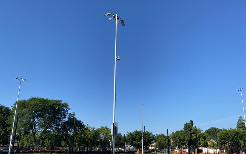 Tall light poles stand against a clear blue sky with green trees in the background.