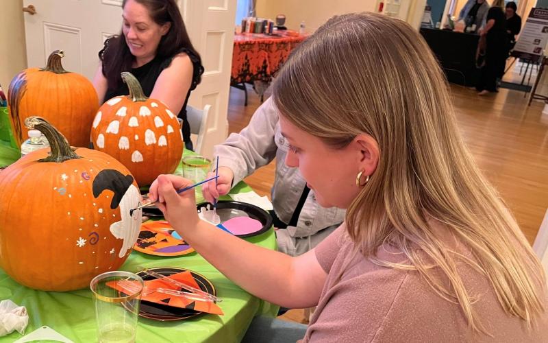 People painting pumpkins at a table.