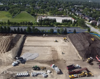 An aerial view of a construction site with heavy machinery, including bulldozers, excavators, and trucks, moving dirt and preparing the ground for a new building.