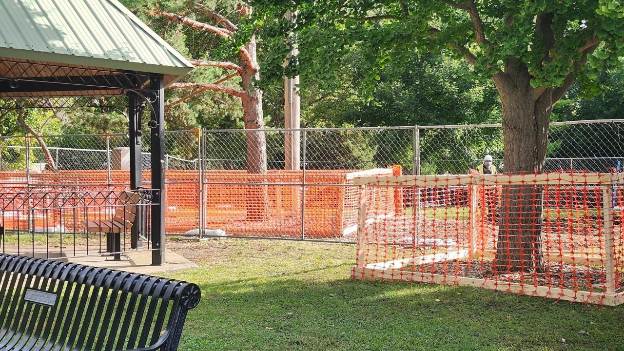 Orange construction fencing in a park. To the left is a green roofed gazebo.