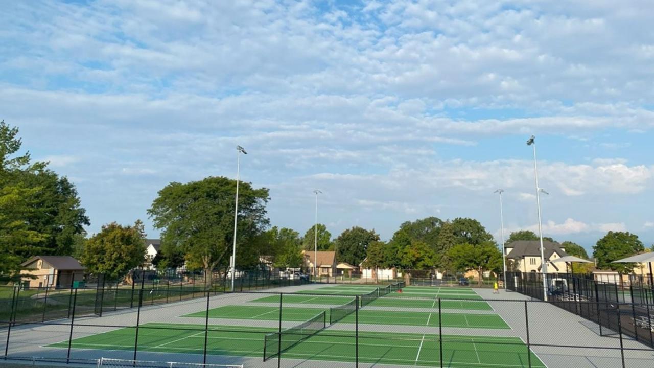 Outdoor sports court with green surface and surrounding chain-link fencing, including several tennis nets.