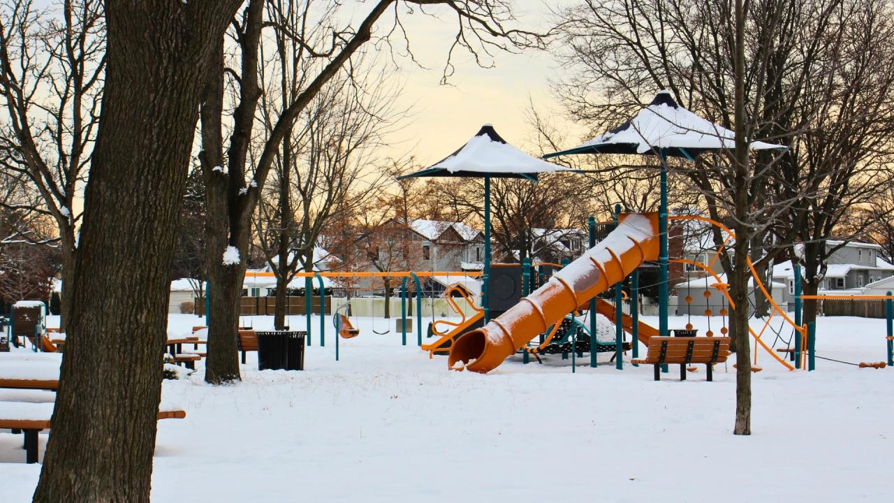 Snow covered playground with the morning sun in the background. Slides and shade structures covered with a dusting of snow. 