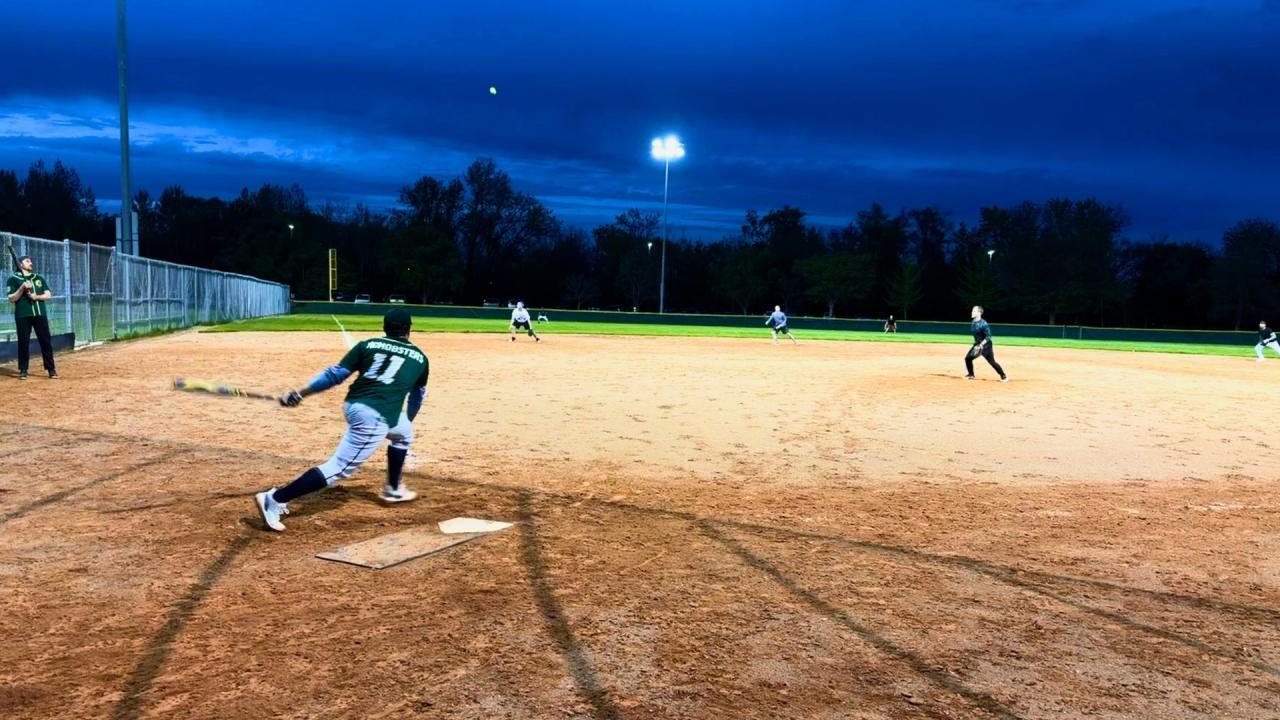A baseball player swings a bat at a ball during a night game under stadium lights.