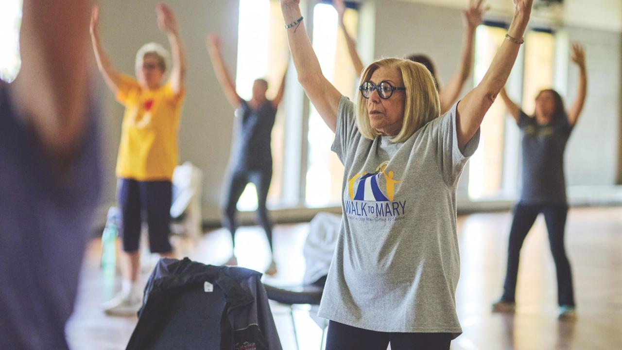 People in a room with their arms raised, participating in an exercise class.