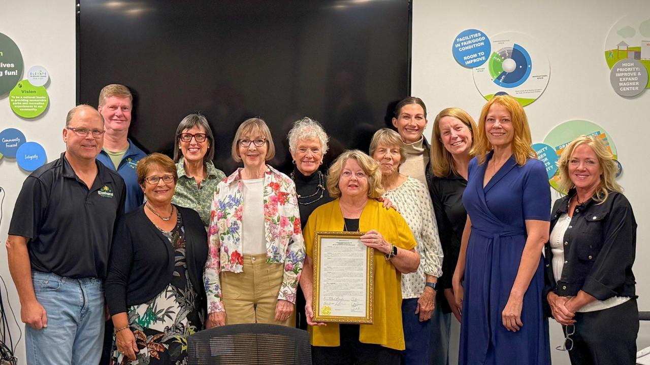Group of adults standing, one person holding a framed certificate while others smile toward the camera.