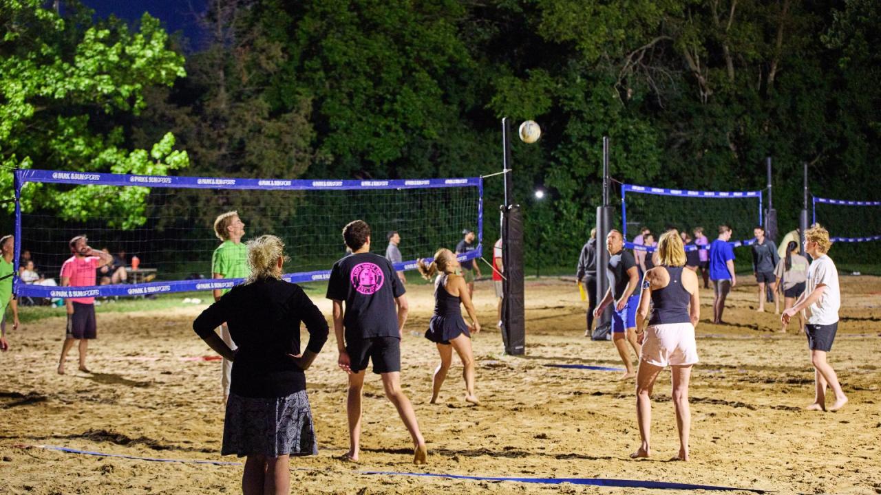 Adults playing sand volleyball at dusk.