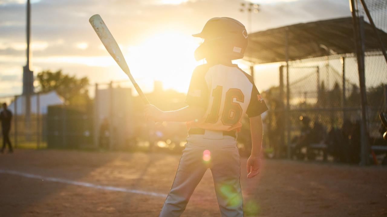A baseball player wearing a helmet and uniform with the number 16 on the back, holding a bat at sunset on a baseball field.