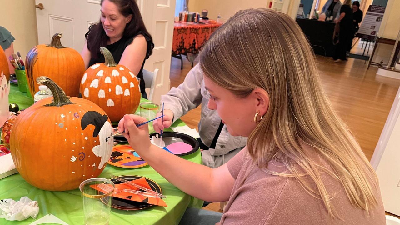 People painting pumpkins at a table.