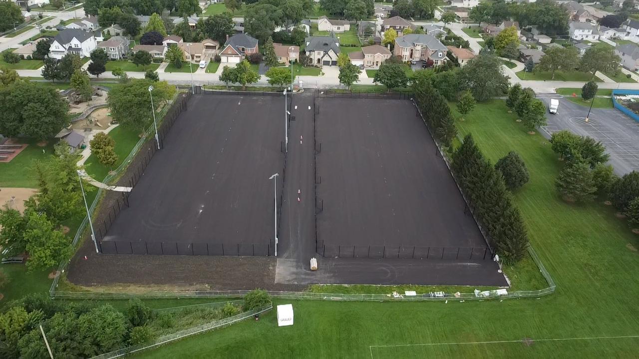Fence fabric and gates installation Aerial view of tennis court asphalt surrounded by a black fence.