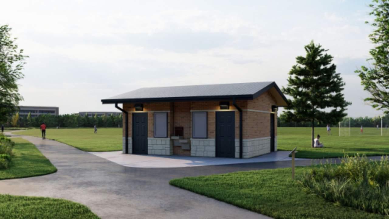 A brick restroom building with two dark doors, a water fountain and billboards