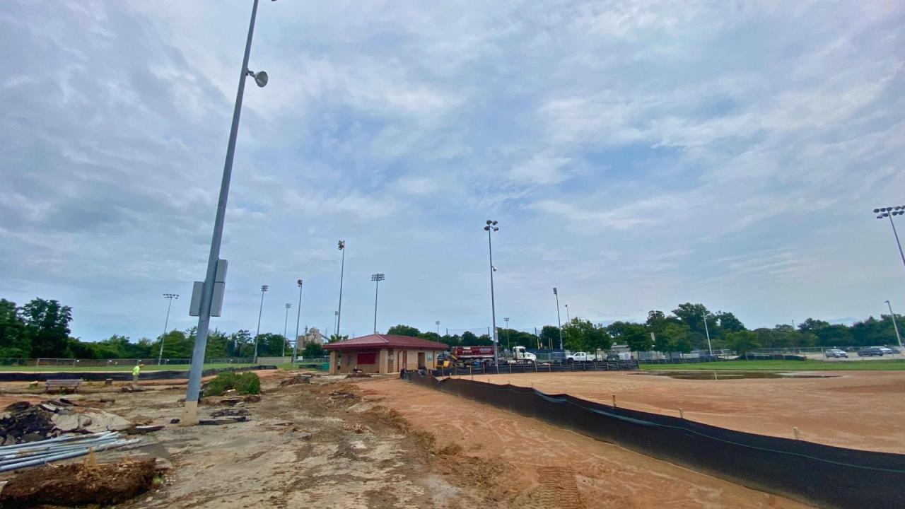 Excavation work at Plunkett Park, August 2026. Construction site at a baseball field, tall light poles, and a small building.